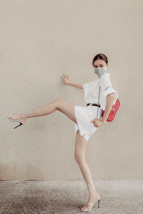 Suit trắng với sự kết hợp của áo hở eo cùng quần short được tăng sức hút với túi hiệu tông đỏ tươi.