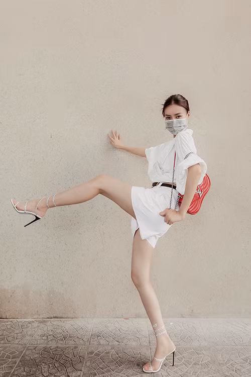 Suit trắng với sự kết hợp của áo hở eo cùng quần short được tăng sức hút với túi hiệu tông đỏ tươi.