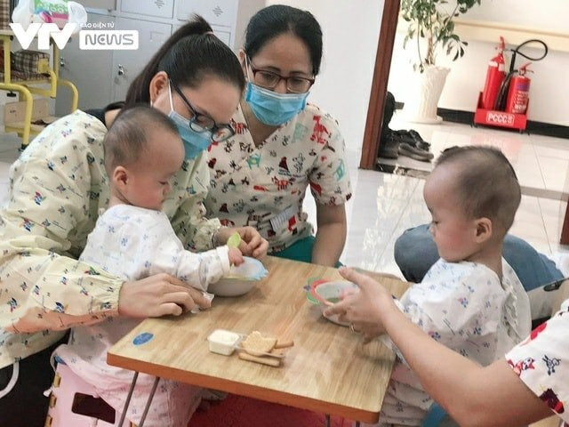 Thay vì nằm ăn thụ động, đút qua bơm truyền, hai chị em tự cầm bình sữa bú, ăn cháo bằng thìa, ngồi ghế ăn đúng tư thế. Ảnh: FBBV, VTV.