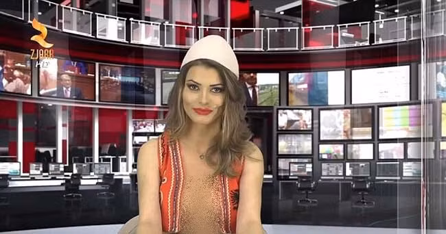 Greta Hoxa cũng mặc mốt "thả rông" như đồng nghiệp cũ, kể cả với áo bình thường hay ghi lê Albania truyền thống trong khi đưa tin trong lễ kỷ niệm Ngày giải phóng.