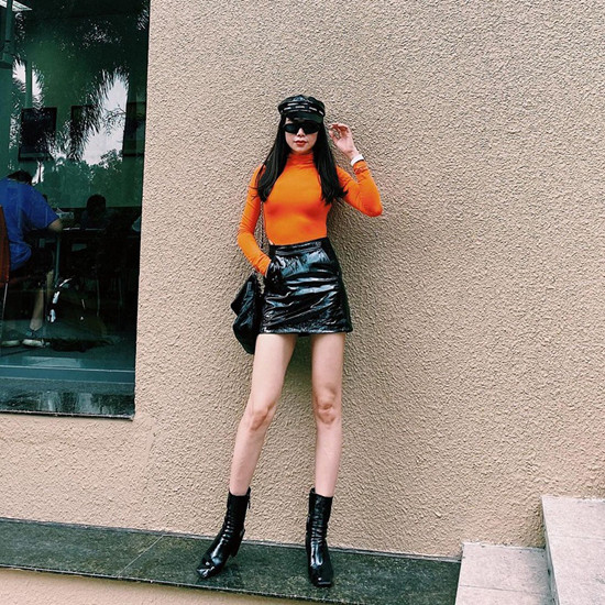 Trà Ngọc Hằng diện set đồ sành điệu với áo cổ lọ tông cam, chân váy da và các phụ kiện da đen bóng bẩy.