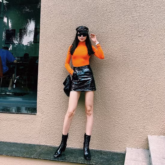 Trà Ngọc Hằng diện set đồ sành điệu với áo cổ lọ tông cam, chân váy da và các phụ kiện da đen bóng bẩy.