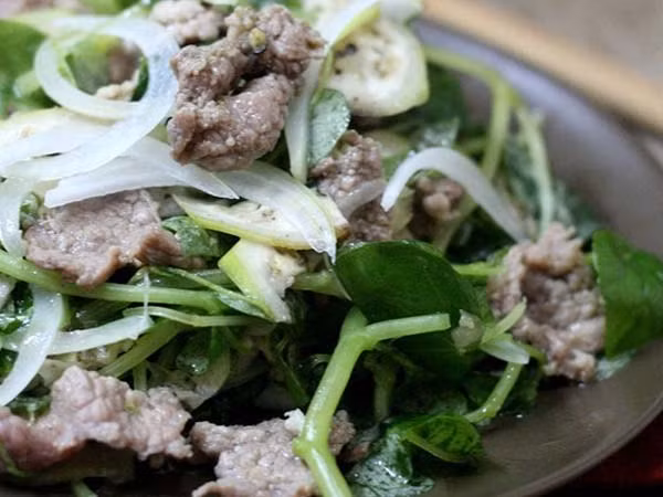 Thịt bò rửa sạch thái mỏng, ướp ít tỏi băm, hạt nêm và dầu ăn cho thấm. Rau càng cua bỏ lá sâu, rửa sạch, ngâm nước muối loãng, vẩy ráo, cho vào thố lớn. Hành tây bóc vỏ, xắt khoanh, cho vào hỗn hợp dầu giấm. Cà chua bi xắt lát. Phi tỏi, cho thịt bò vào thố rau, chan nước dầu giấm, hành tây và cà chua bi vào cùng.