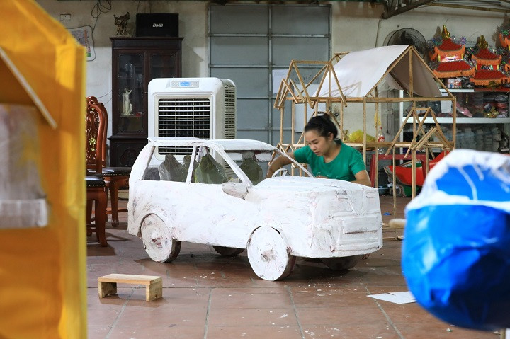 Sân nhà của một người dân làm vàng mã tại Phúc Am chất đầy nguyên liệu để sản xuất mặt hàng đặc thù phục vụ ngày Rằm tháng 7. Ngoài những sản phẩm quen thuộc như quần, áo, người làm vàng mã tại Phúc Am còn nhận đặt hàng sản xuất những mẫu mã mới theo yêu cầu của khách hàng. Trong ảnh, thợ sản xuất đang hoàn hiện chiếc ô tô bằng vàng mã.