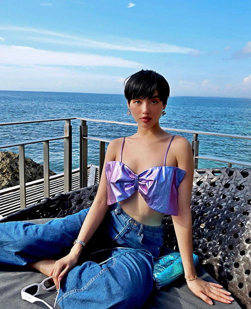 Trong chuyến du lịch biển, Khánh Linh nổi bật với chiếc áo đính nơ kiểu hai dây ánh kim tông tím lãng mạn mix cùng quần jeans ống suông.