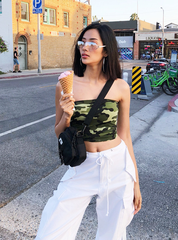 Á hậu Hoàng Thùy với hình ảnh năng động khi diện áo quây họa tiết camo đi cùng túi đeo chéo, quần dây rút và các phụ kiện kính mắt, hoa tai hợp mốt.
