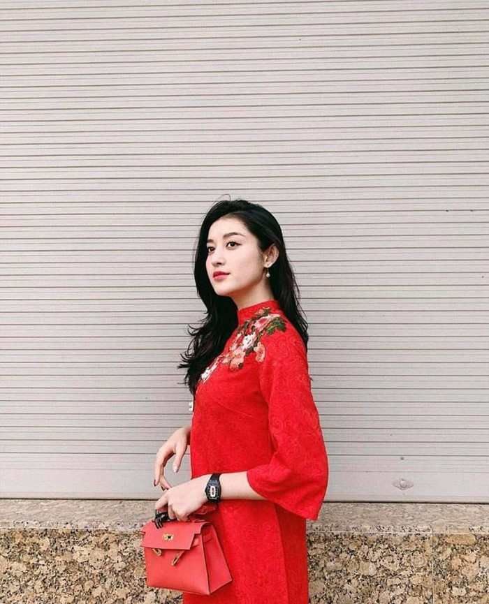 Á hậu Huyền My diện áo dài đỏ có chi tiết hoa thêu nổi trên vai áo để tạo điểm nhấn cho tổng thể trang phục, nhất là khi cô đã chọn thêm một chiếc túi xách đỏ làm phụ kiện cho mình.