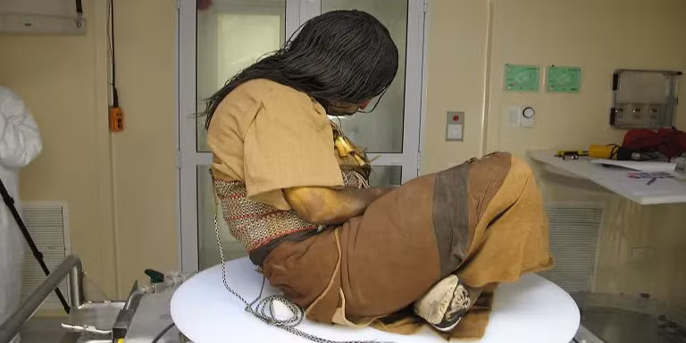 Thiếu nữ này được lựa chọn từ năm 12 tuổi để làm vật tế thần, sống xa cha mẹ và chuẩn bị cho nghi lễ hiến tế. Vài tuần cuối đời, cô được cho uống rượu và sử dụng lá cocaine để giảm đau và chuẩn bị cho cái chết.