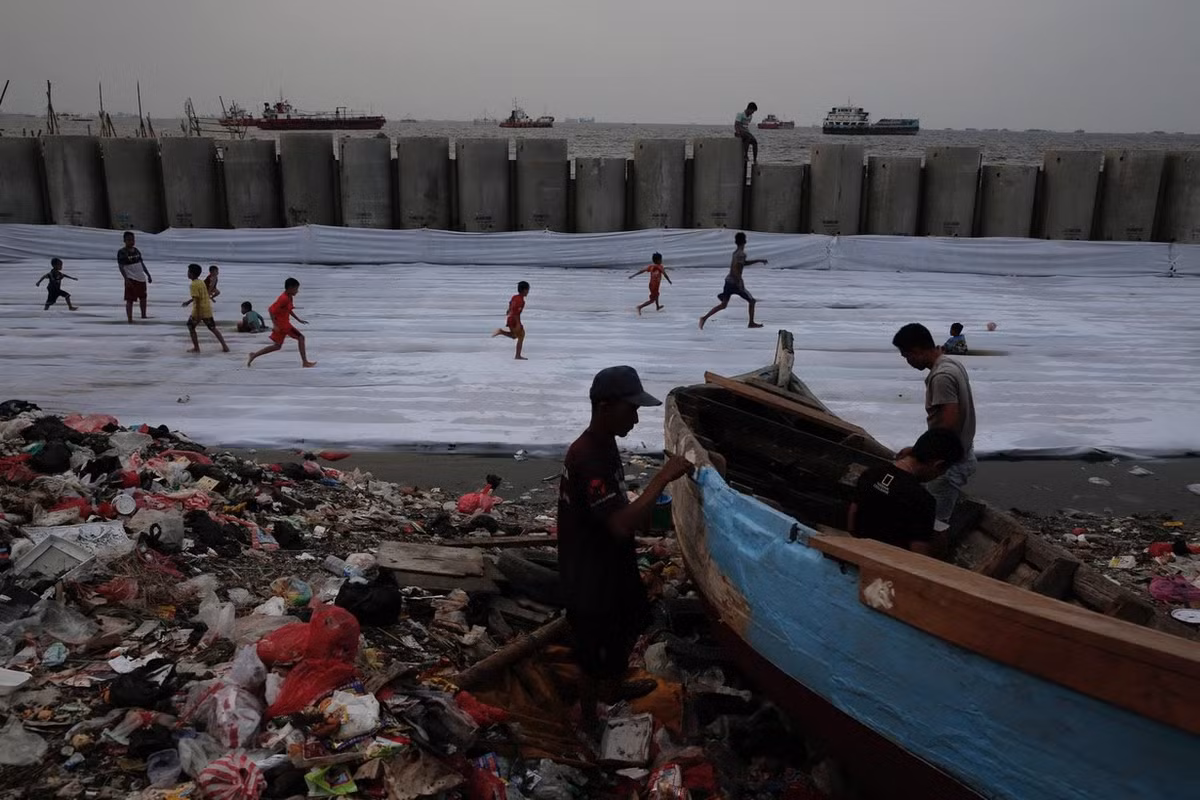 Thế nhưng với tốc độ sụt lún như hiện nay, các chuyên gia cảnh báo toàn bộ tường biển cũng có thể bị chìm dưới nước trong chỉ hơn một thập kỷ nữa. Trong ảnh, ngư dân sửa chữa tàu cá hỏng và trẻ em chơi đùa bên một đoạn tường biển, giải pháp tạm thời để cứu lấy Jakarta khỏi triều cường và xói mòn do nước biển.