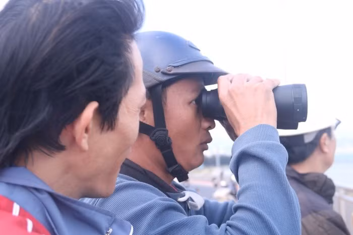 Một người dân tập trung cao độ vào việc quan sát tàu sân bay bằng ống nhòm. Bên cạnh, một người dân khác đang chờ đến lượt mình được xem. Ảnh Nguyễn Thành