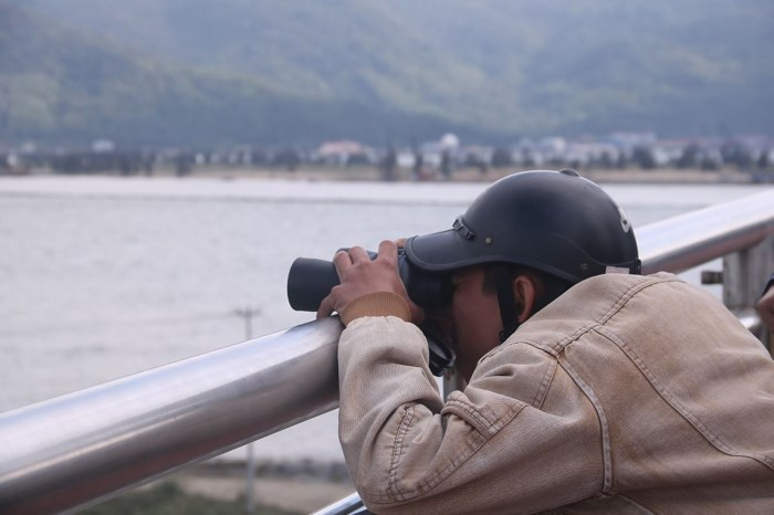 Để quan sát rõ nét tàu sân bay, một người dân kê ống nhòm lên làn can cầu để lấy nét và điều chỉnh cự ly quan sát. Quy mô, kích thước cũng như số lượng máy bay chiến đấu trên tàu sân bay USS Carl Vinson khiến người dân không khỏi thích thú và choáng ngợp. Ảnh Nguyễn Thành