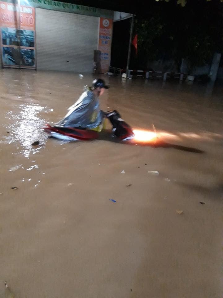 Một người đang bì bõm dắt xe dưới đường ngập nước.