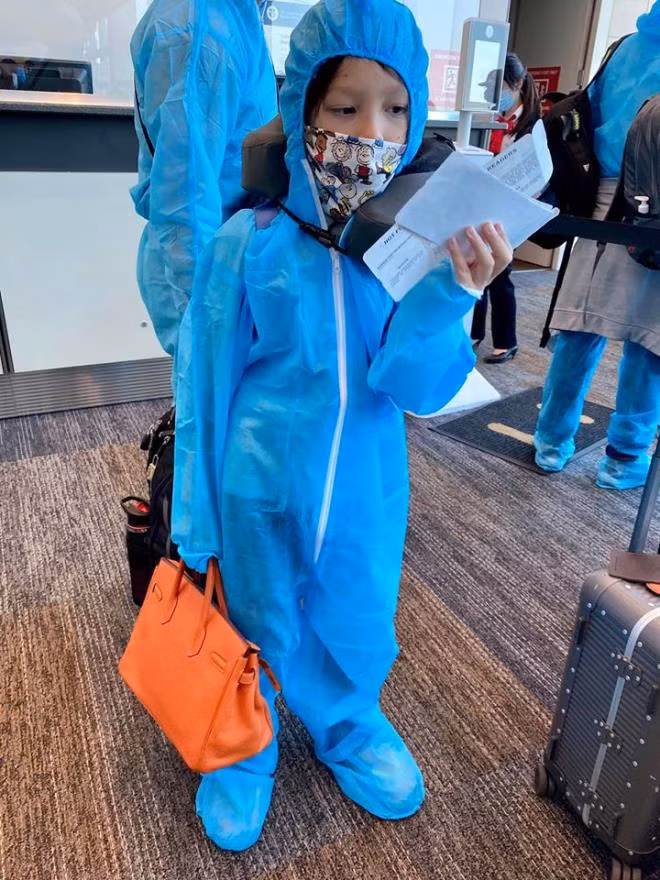Hình ảnh các con của Hồng Nhung khi lên máy bay về Việt Nam. Bé Tôm gọi bộ trang phục bảo hộ là "bộ đồ phi hành gia".