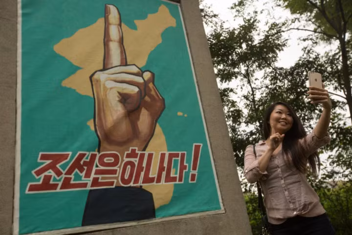 Một nữ du khách Mỹ chụp ảnh trước tấm biểu ngữ tại Khu phi quân sự tại Triều Tiên.