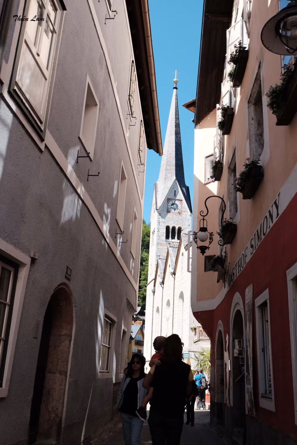 Từ bus 150 rồi chuyển sang tàu, tổng thời gian mất khoảng hơn hai tiếng rưỡi di chuyển. Ngay khi xuống tàu, bạn sẽ thấy chỉ dẫn đến bến bắt phà qua làng Hallstatt. Hallstatt từ xa đã toát lên vẻ phong thủy hữu tình, những ngôi nhà cổ tựa núi, hướng ra hồ. Cái nắng dễ chịu khiến thị trấn nhỏ được phản chiếu, lung linh hơn dưới làn nước xanh ngắt của hồ Hallstattersee. Từ bến phà, đi dọc con đường chính, bạn sẽ bắt gặp nhà thờ cổ...