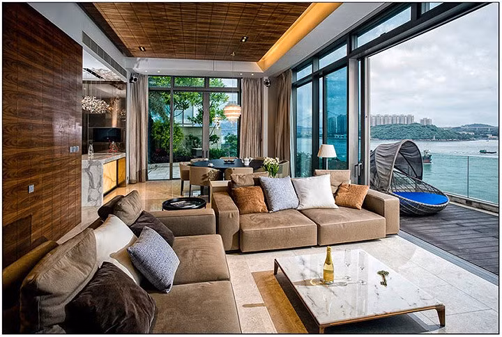 Phòng khách với đồ nội thất tiện nghi và nhìn ra bên ngoài. Mặt tiền sử dụng cửa kính trượt lớn, khiến ngôi nhà đẹp long lanh và tràn ngập ánh sáng.