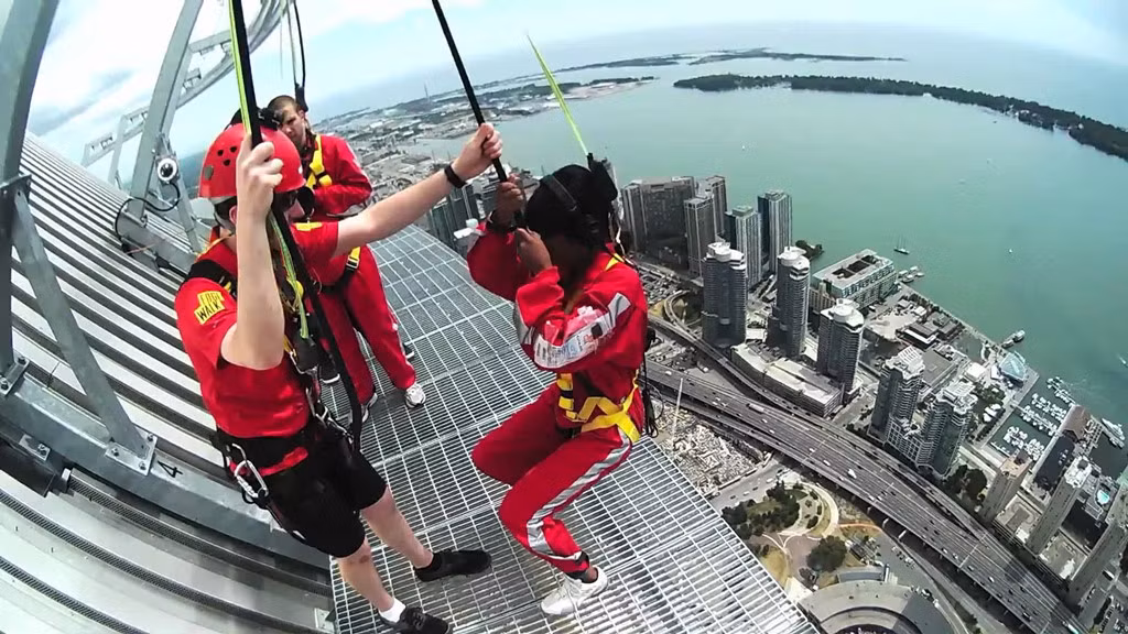 CN Tower ở Canada là địa điểm thu hút du khách trải nghiệm cảm giác lạ khi đứng ở mép của đường đi bộ Edge Walk tại độ cao 365 m so với mặt đất. Du khách được đảm bảo an toàn bằng dây đai kết nối với móc tròn trên thắt lưng. Ảnh: Youtube.