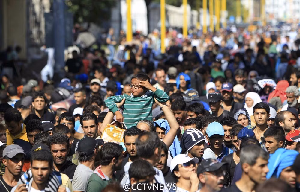 Một cậu bé được bố cõng đi trong dòng người nhập cư.