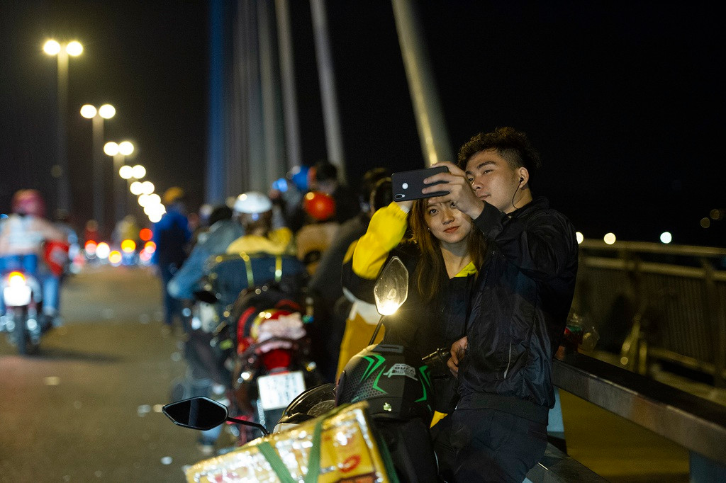Gần 0h 28 Tết, đôi bạn trẻ đi từ hướng Tiền Giang về Vĩnh Long dừng ở cầu Mỹ Thuận tạo dáng chụp ảnh. Dù đã khuya, vẫn có hàng trăm người đứng ở đây để nghỉ ngơi, trò chuyện. Phần lớn là dân lao động và sinh viên đang học tập, làm việc ở TP.HCM hoặc nhiều tỉnh thành lân cận về quê ăn Tết.