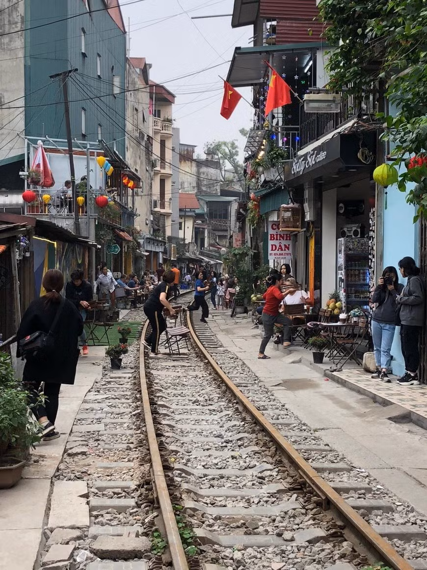 Mỗi khi có chuyến tàu chạy qua, nhiều chủ quán cà phê và du khách lại cầm bàn, ghế chạy ra khỏi đường tàu. (Ảnh: Vi Thương - Hải Yến/TTXVN).