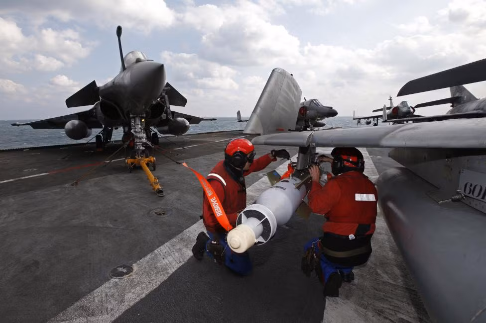 Phi hành đoàn lắp trang thiết bị lên chiếc phản lực cơ Super Etendard trên tàu sân bay Charles de Gaulle ngày 29/1. Cạnh đó là chiến đấu cơ Rafale.