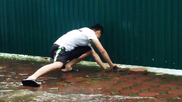 Nam thanh niên này nhanh tay bắt lấy con cá sau khi cá nhảy theo nước tràn từ phía bên trong ao nước của một công trình ra phía vỉa hè đường Mễ Trì.