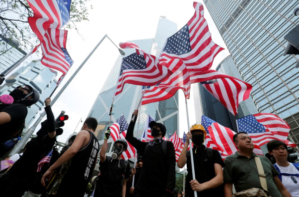 Đám đông người biểu tình mang theo ô, cờ Mỹ và các biểu ngữ trên đường tiến về phía lãnh sự quán Mỹ.