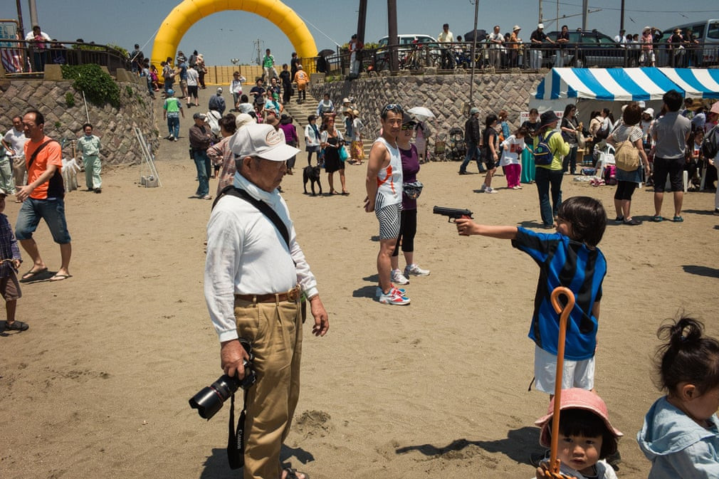 Khoảnh khắc được nhiếp ảnh gia Shin ghi lại ở bãi biển Yuigahama vào tháng 5/2012. "Mọi người tham gia lễ hội ở đây không nhận ra điều này. Một đứa trẻ đang chạy quanh, tay cầm khẩu súng đồ chơi. Cuối cùng, cậu bé tìm được một mục tiêu, là người đàn ông cao tuổi này, cũng đang cầm một 'khẩu súng' khác", ông Shin miêu tả lại.