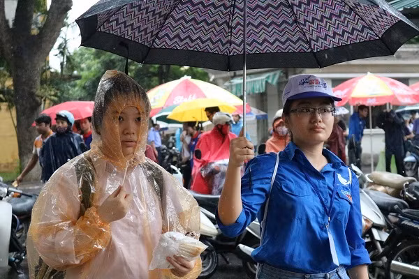 Một thí sinh đến làm thủ tục dự thi muộn được nữ tình nguyện viên che ô dẫn lên phòng dự thi.