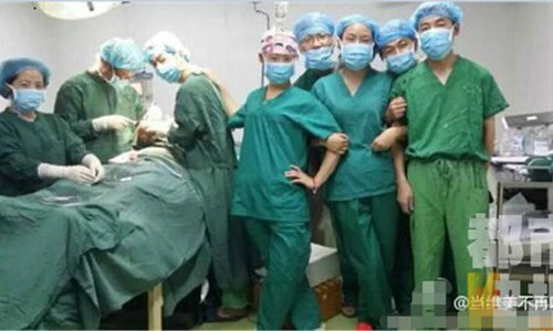 Ba bác sĩ đang khâu vết thương cho bệnh nhân, trong khi những người khác đứng tạo dáng để chụp ảnh ngay bên bàn mổ.