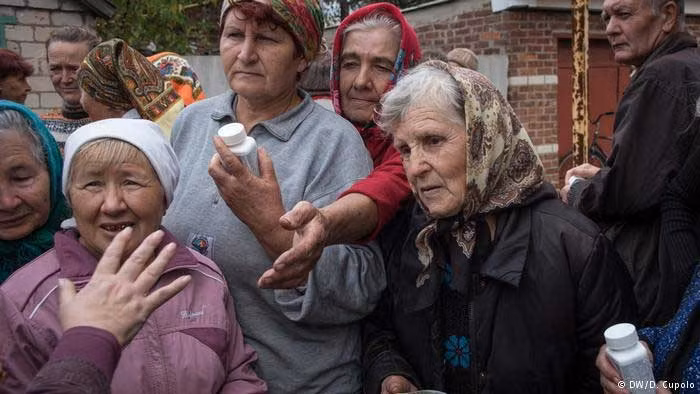 Các bà nội trợ đang đứng chờ nhận thuốc và vitamin. Đồ ăn và đồ cứu trợ sẽ được chuyển tới thị trấn Ukraine này bởi các tổ chức từ thiện. Người dân ở đây có khi phải đứng xếp hàng cả ngày để nhận đồ cứu tế do các đoàn xe mất thời gian để vượt qua các trạm kiểm soát. Ảnh DW