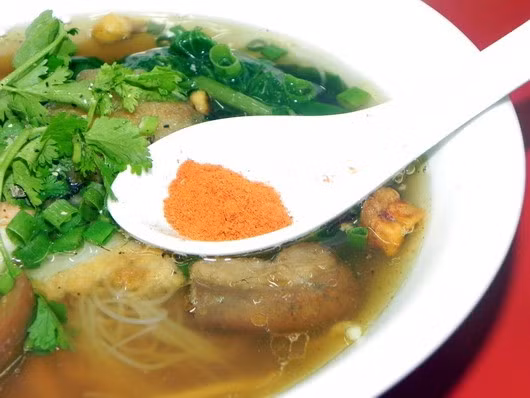 Mì tôm Singapore hấp dẫn với màu trắng của sợi hủ tíu ẩn dưới màu vàng ươm của mì, con tôm đỏ au, miếng lòng khía nước dừa màu cánh gián, cùng loại rau có hình dáng giống rau muống nhưng vị như rau cần tây.