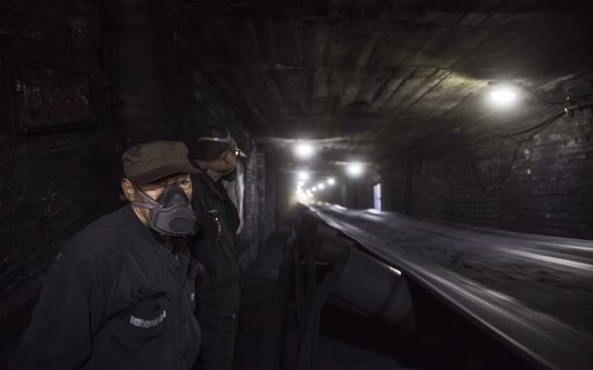 Người công nhân đeo mặt nạ theo dõi việc vận chuyển than đá trên một băng chuyền.