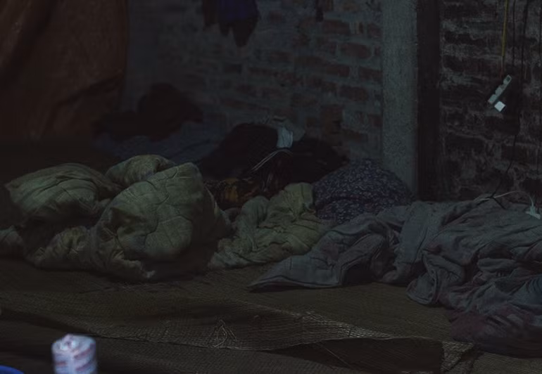 Chăn chiếu lộn xộn trên giường ở góc tường tối tăm và ẩm.