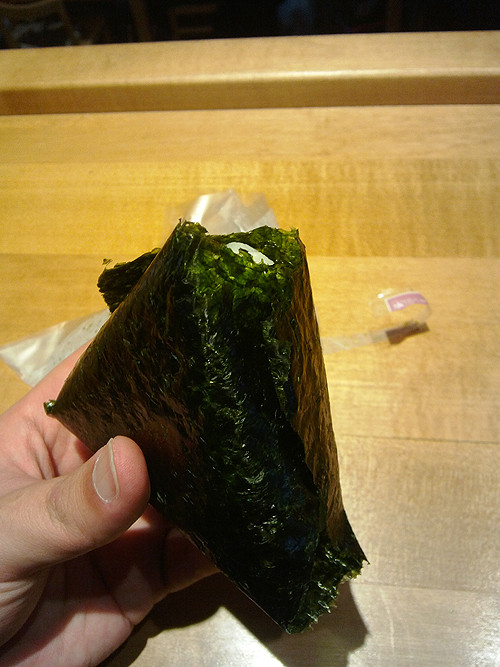 Gập tiếp miếng rong biển sao cho phủ kín mặt còn lại của miếng cơm, có thể phết thêm dầu mè và rắc thêm vừng để tăng thêm mùi vị nhé.