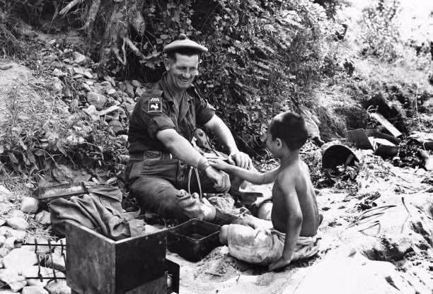 Một bé trai ngồi bên cạnh một binh sỹ người Scotland ở khu vực do Anh phụ trách ở sông Nakdong, Hàn Quốc, ngày 13/9/1950.