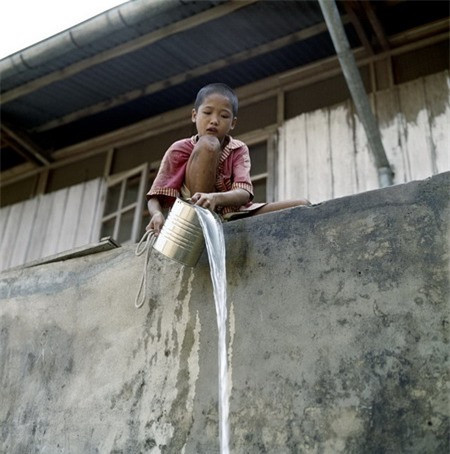 Cậu bé múc nước bằng xô thiếc.