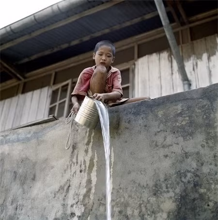 Cậu bé múc nước bằng xô thiếc.