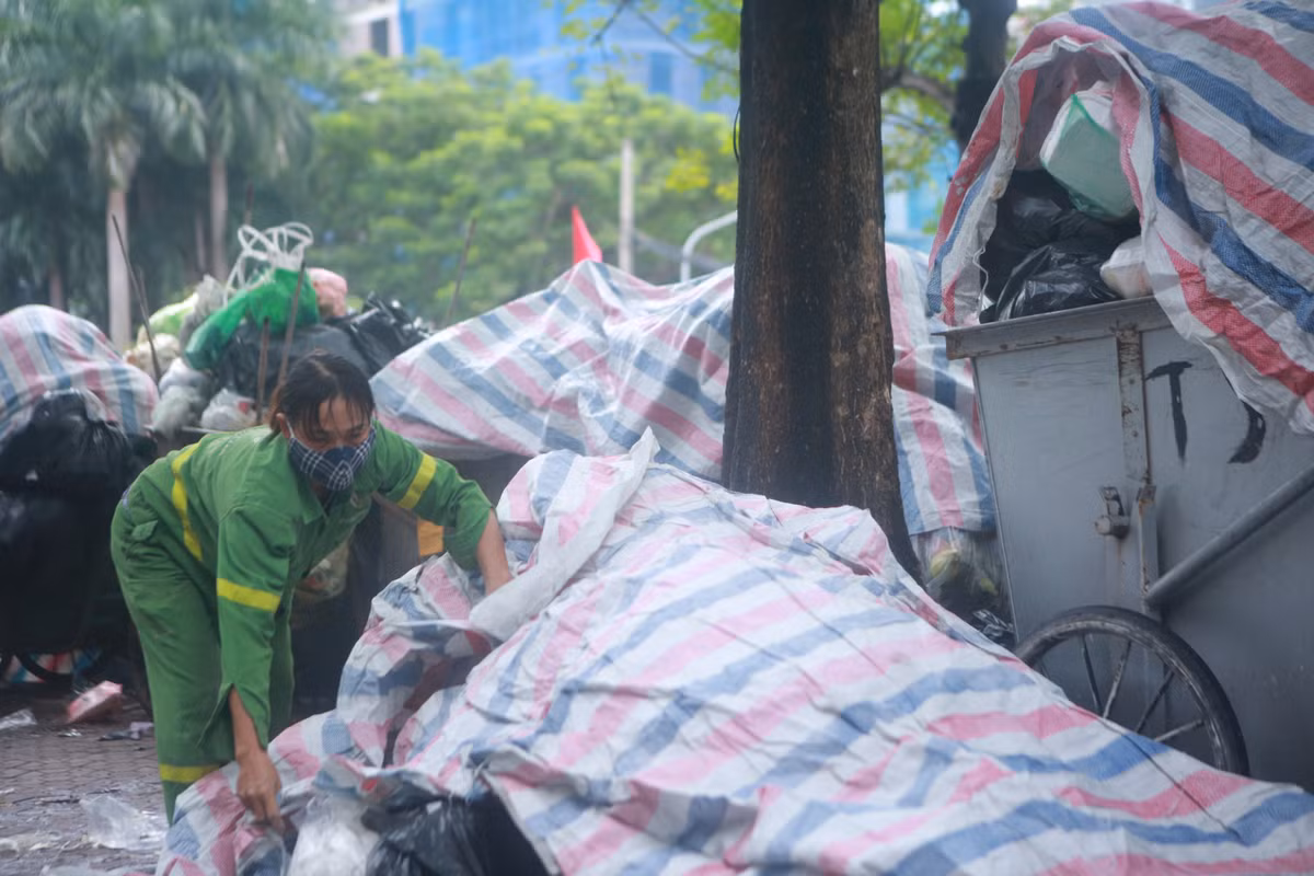 Để hạn chế mùi hôi bốc lên, nhân viên vệ sinh môi trường đã phải dùng bạt lớn phủ lên các xe rác.