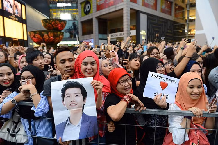 Người hâm mộ Malaysia giơ hình ảnh thần tượng. Dễ dàng nhận ra có rất nhiều người hâm mộ lớn tuổi xếp hàng chờ đón.
