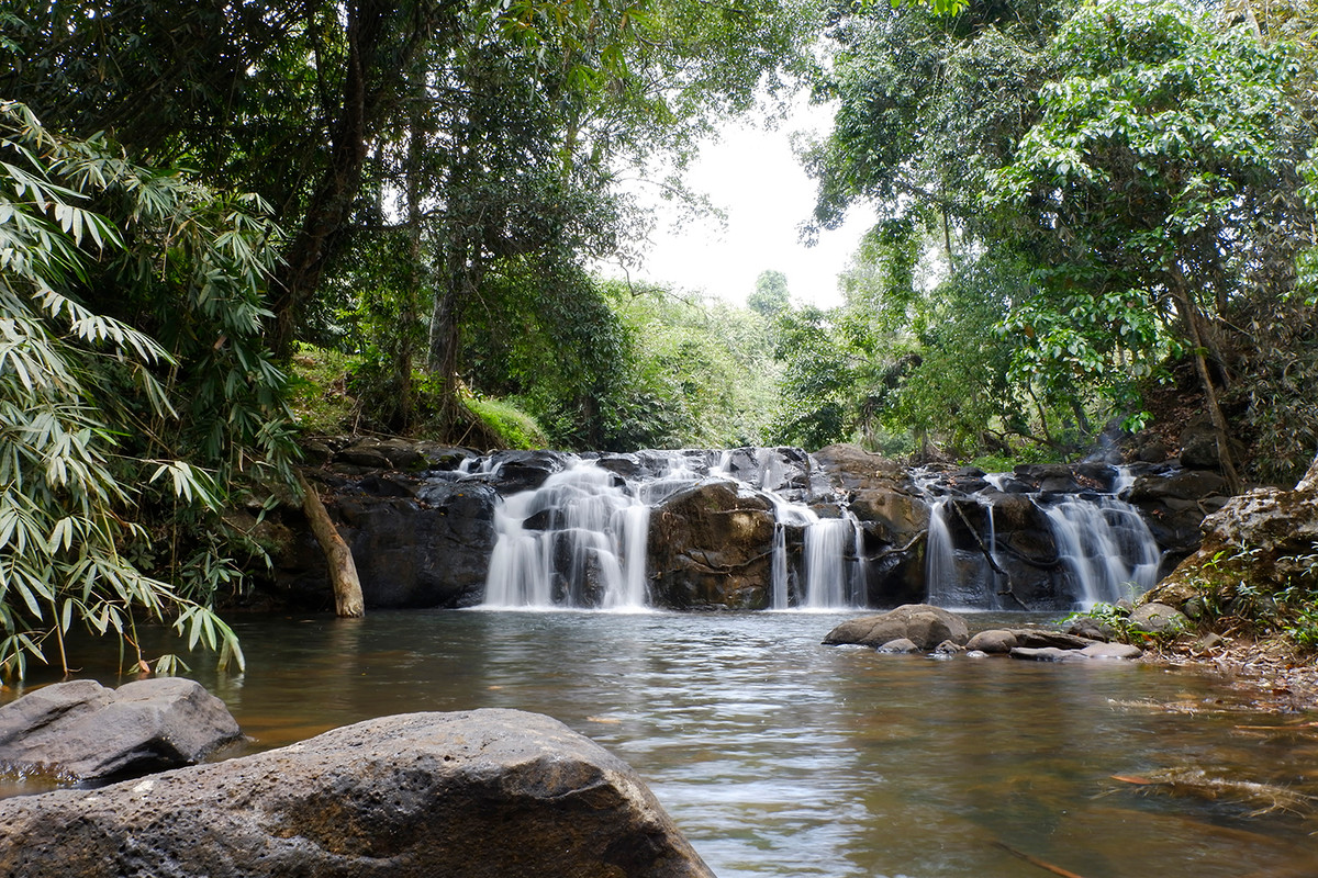 Từ chùa Di Đà, men theo con đường nhỏ dẫn lối, bước xuống những bậc thang bằng đá trát xi măng mộc mạc, ngang qua vườn cà phê và cây ăn trái, đầu tiên du khách sẽ bắt gặp thác Quan Âm thấp thoáng sau rặng cây.