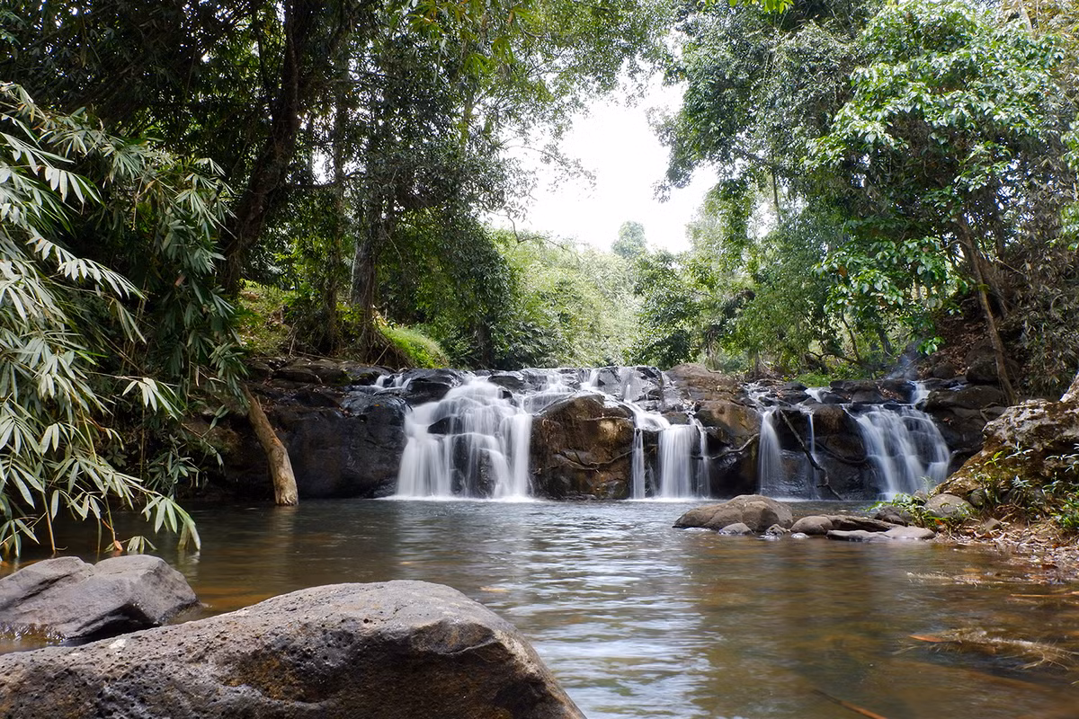 Từ chùa Di Đà, men theo con đường nhỏ dẫn lối, bước xuống những bậc thang bằng đá trát xi măng mộc mạc, ngang qua vườn cà phê và cây ăn trái, đầu tiên du khách sẽ bắt gặp thác Quan Âm thấp thoáng sau rặng cây.