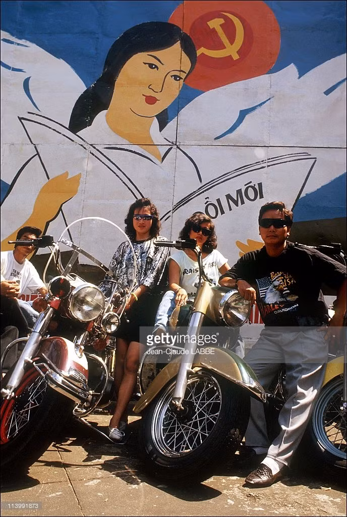 Những người chơi xe Harley Davidson trước một pa-nô cổ động cho công cuộc Đổi Mới.