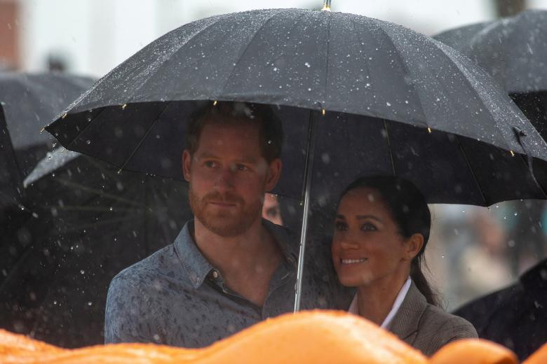 Hoàng tử Harry và Công nương Meghan Markle che ô chung dưới trời mưa khi tham dự một sự kiện ở Công viên Victoria, Dubbo, ngày 17/10.