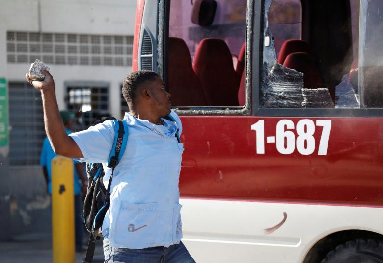 Một người biểu tình ném đá vào chiếc xe buýt tại thủ đô Haiti.