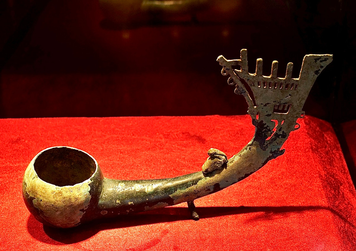 Muôi đồng dáng tẩu, cán muôi hình mũi thuyền rồng, trên thân cán có tượng bồ nông. Niên đại thế kỷ 3-1 TCN.