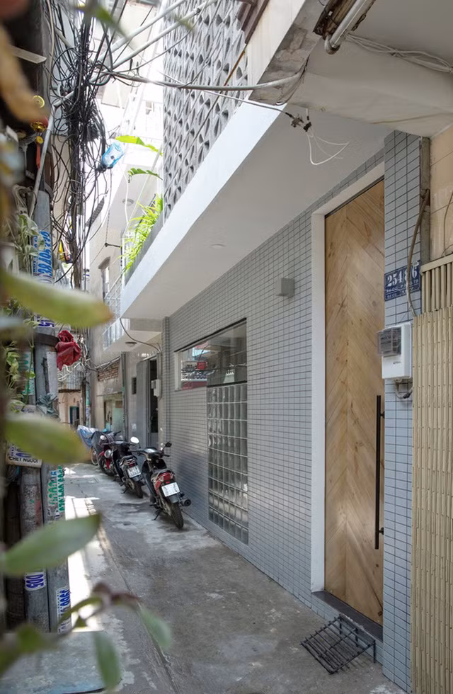 Cửa gỗ nâu sáng, kết hợp cùng tường màu xám nhạt với ô cửa kính khiến căn nhà thoáng mát hơn.