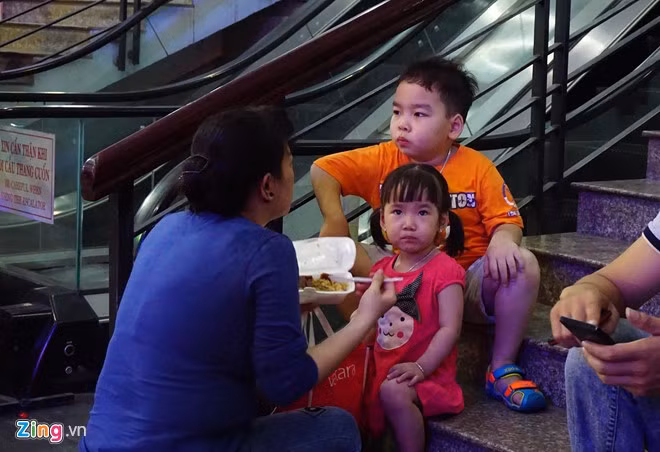 Một bà mẹ đang cố gắng cho hai con ăn “được muỗng nào hay muỗng nấy” trong lúc chờ tàu.