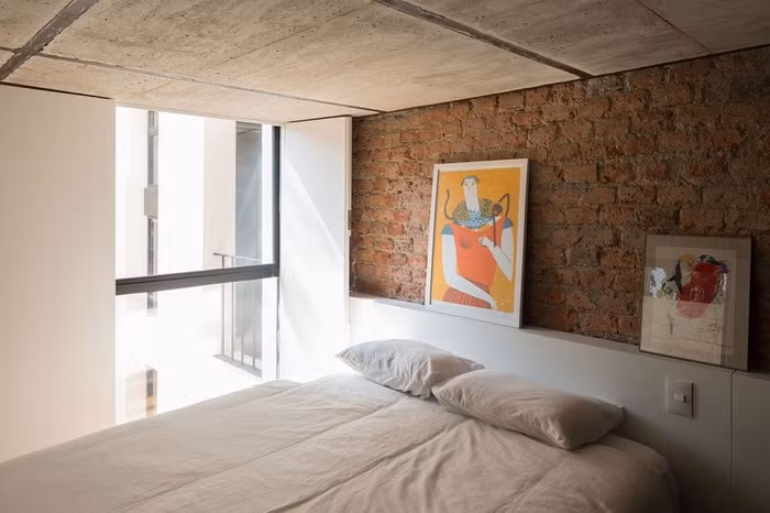 Phòng ngủ được ưu ái ở vị trí có cửa sổ nhìn ra ban công, nơi ngập tràn ánh sáng tự nhiên. Để không gian nghỉ ngơi rộng rãi và thoáng sáng, các kiến trúc sư đã sử dụng chủ yếu gam màu trắng cho tường, chăn ga gối. Thêm điểm nhấn cho không gian với bức tường gạch trần đơn giản.