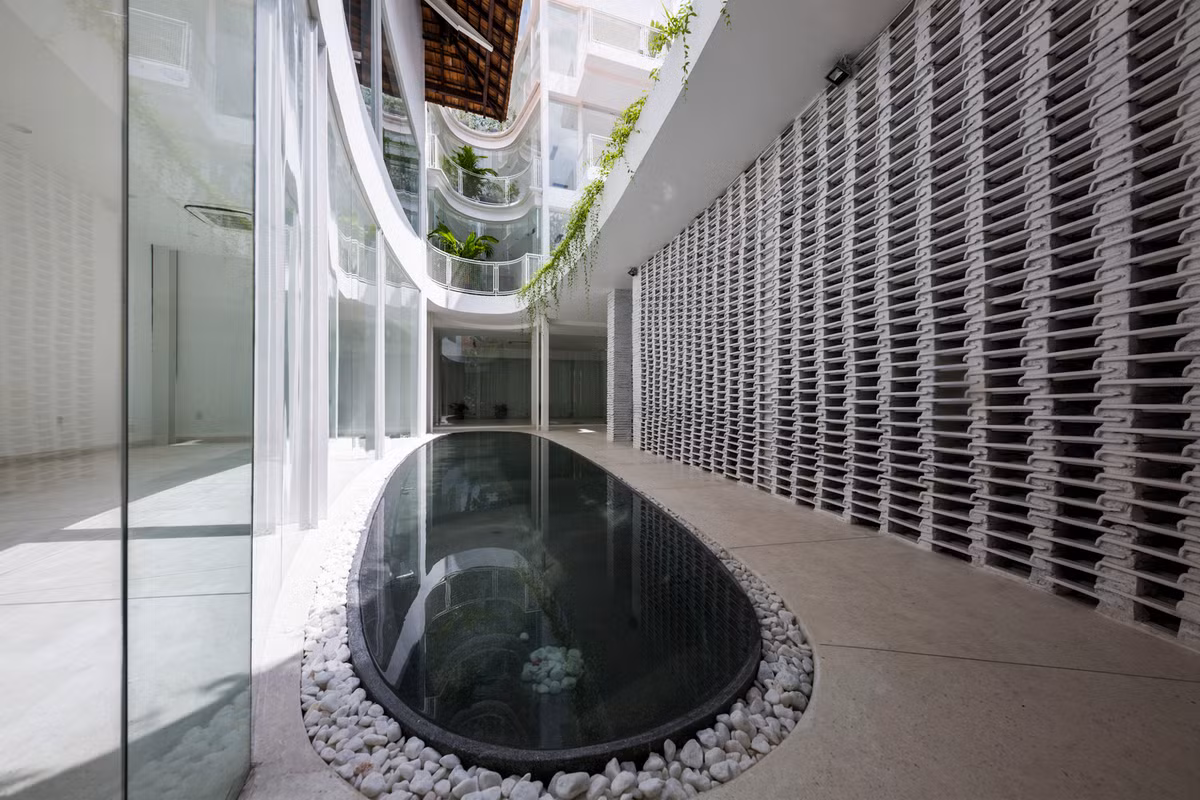 Hồ bơi lớn đặt giữa nhà, được bao quanh bởi rất nhiều viên đá nhỏ. Bức tường đục lỗ xếp chồng lên nhau lạ mắt.